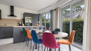 A modern kitchen with a dining area, large windows, and a view of the outdoors.