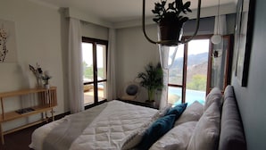 Ein Schlafzimmer mit Bett, Nachttisch, Stuhl, Fenster und Blick ins Freie.