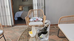Ein Zimmer mit Korbmöbeln, einem Bett mit Kopfteil, einer Weinflasche und einem Glas auf einem Tisch.