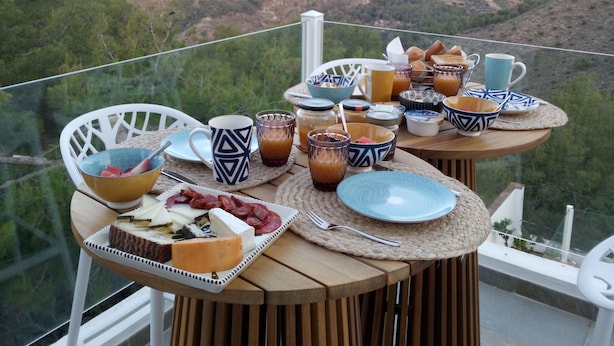 Ein Tisch mit verschiedenen Speisen und Getränken auf einem Balkon mit Blick auf eine Berglandschaft.