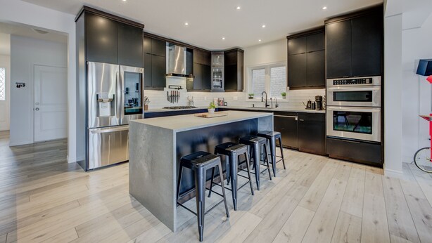 A modern kitchen with a central island, bar stools, stainless steel appliances, and dark cabinetry.