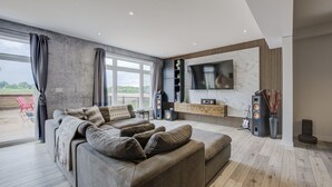 A modern living room with a large grey sofa, a flat-screen TV, and a wooden entertainment unit.