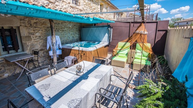 A stone building with a hot tub, outdoor seating, and a table with chairs. - Gîte Standing Avec Jacuzzi Privatif (Allègre-les-Fumades)