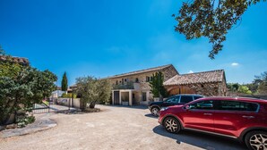 A two-story stone house with a tiled roof, a paved driveway, and a red car parked in the foreground. - Gîte Standing Avec Jacuzzi Privatif (Allègre-les-Fumades)