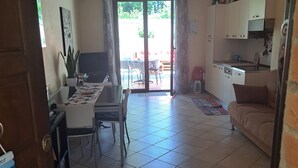 Amplia sala de estar con mesa y sillas de comedor, cocina con armarios y encimera, y puerta corrediza de vidrio que da a un patio exterior.