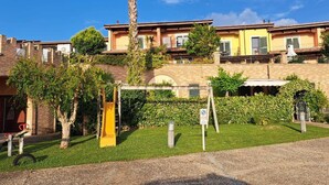 Un edificio residencial con fachada de ladrillo, puerta amarilla y un pequeño jardín con un tobogán amarillo.