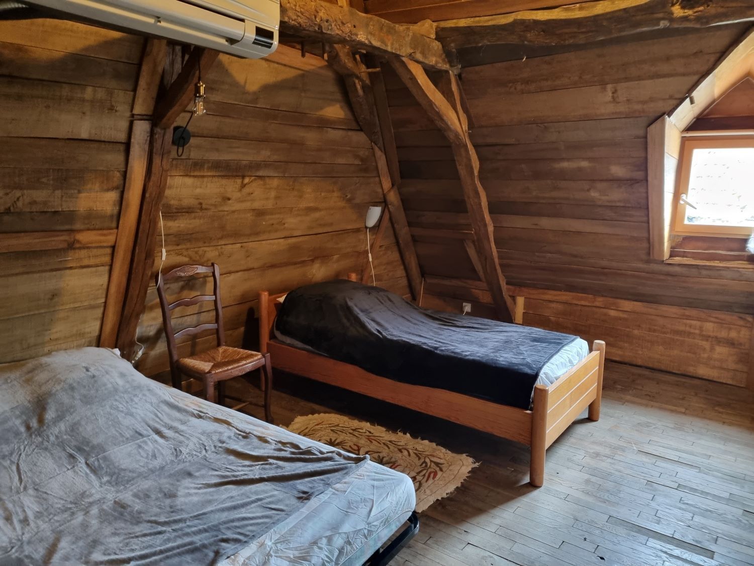 Une pièce rustique aménagée dans une cabane en bois, avec un lit en mezzanine, une chaise et une petite fenêtre.