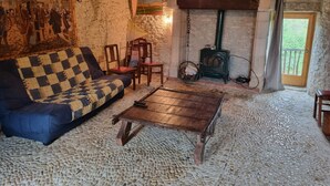 Ein rustikaler Raum mit einem karierten Sofa, Holzstühlen, einem Holztisch, Steinböden, einer Steinwand, einem Holzofen und einem Gemälde.