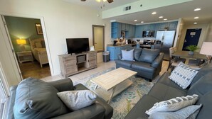 A living room with a sofa, coffee table, and a television on a stand. - Splash 906E -Master on Gulf-Free Golf & Activities Daily! (Panama City Beach)