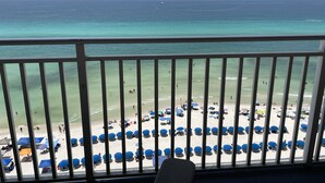A balcony with a view of a beach with blue umbrellas and people. - Splash 906E -Master on Gulf-Free Golf & Activities Daily! (Panama City Beach)