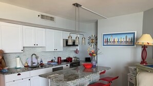 A kitchen with white cabinets, a granite countertop, a built-in island with red bar stools, a red kettle, and a vase with flowers. - Spectacular Direct Beach ,Ocean  View 17 floor Romantic Get Away King Bed ! (Myrtle Beach)