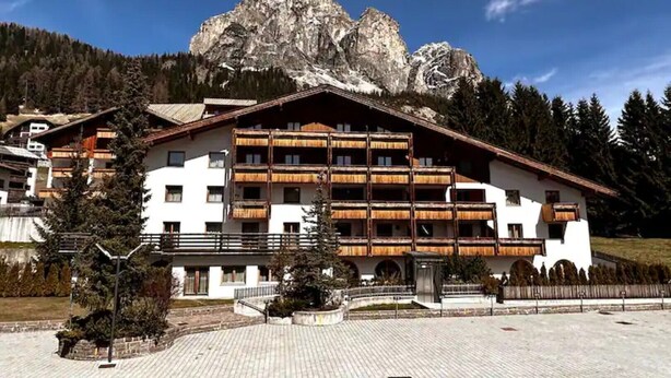 A multi-story hotel with balconies, set against a mountainous backdrop. - The perfect retreat for those seeking peace, comfort, sports and nature (Corvara in Badia)