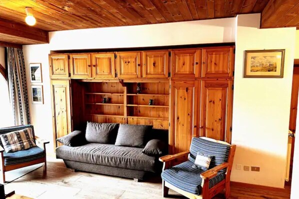 Un salon chaleureux avec un plafond en bois, un canapé, un fauteuil à rayures et des étagères intégrées en bois.