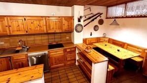 A kitchen with wooden cabinets, a sink, a dishwasher, and a dining area with benches. - The perfect retreat for those seeking peace, comfort, sports and nature (Corvara in Badia)