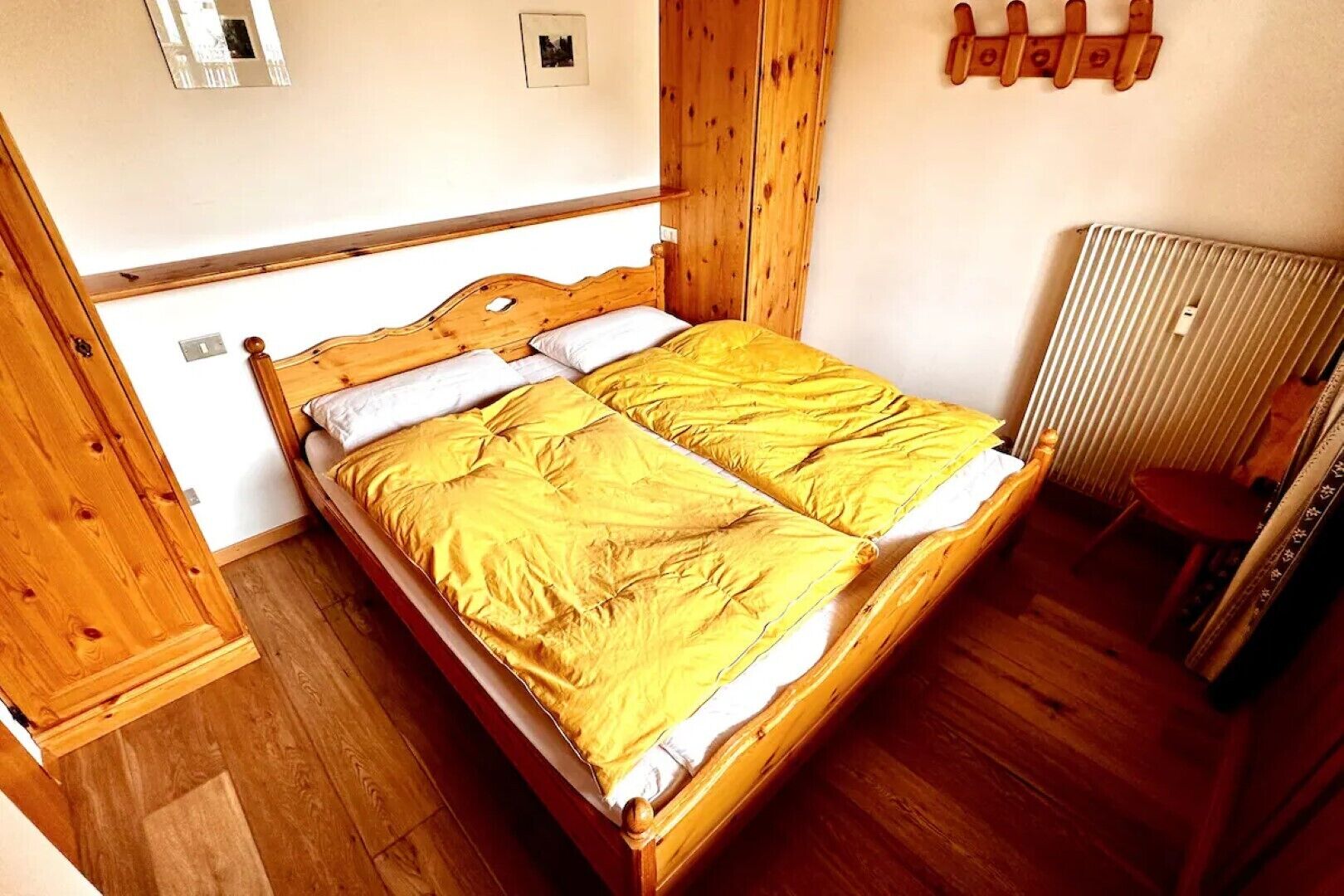 A wooden bed with a white mattress and yellow bedding in a room with wooden floors and a radiator.