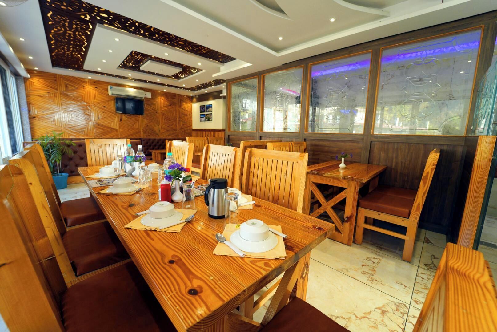 A restaurant with wooden furniture, a long table set for dining, and a large window with a view.