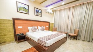 Une chambre d’hôtel avec un grand lit, une table de chevet, une chaise, un bureau et une fenêtre avec des rideaux.