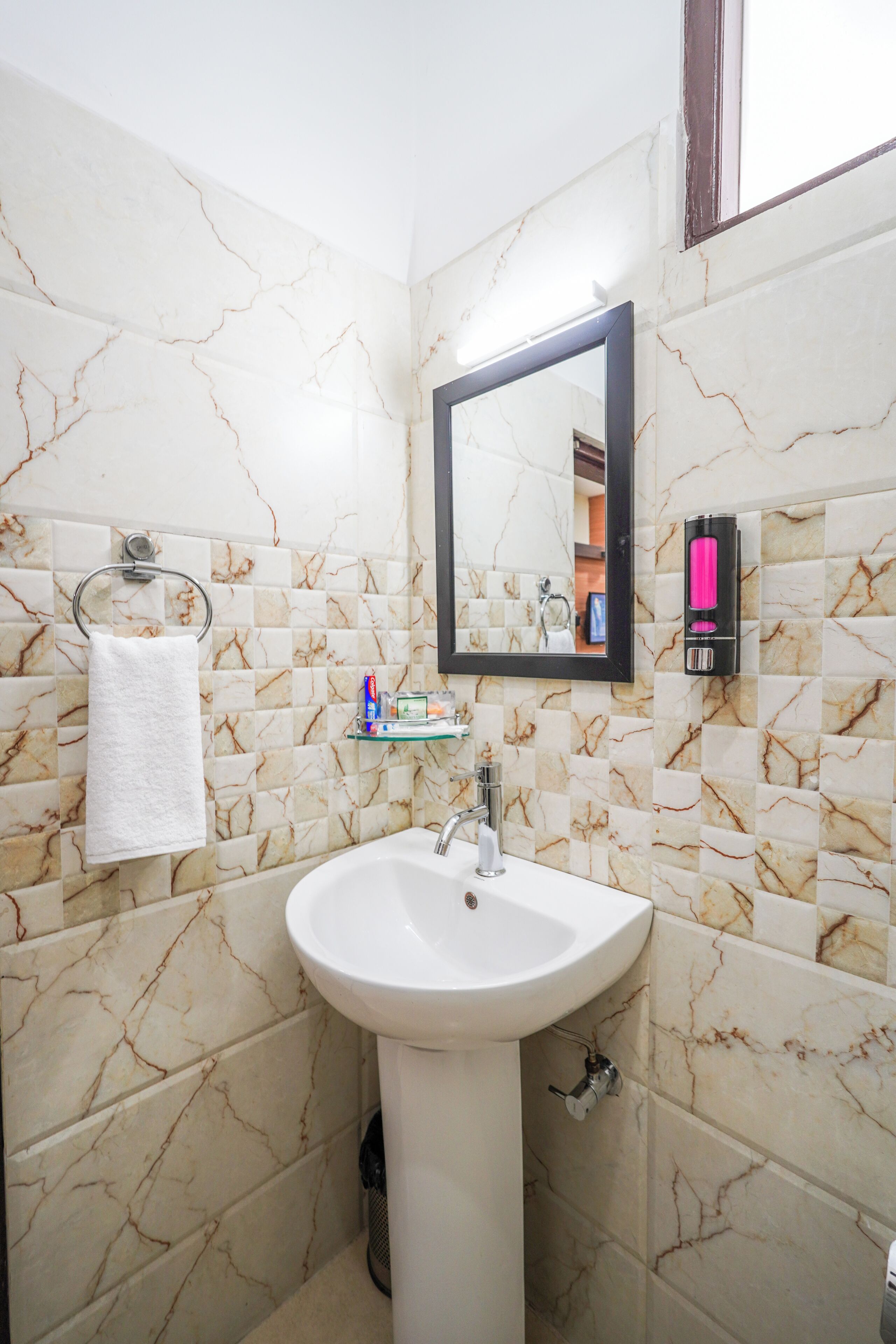 A bathroom with marble walls, a sink, a mirror, a towel rack, and a soap dispenser.