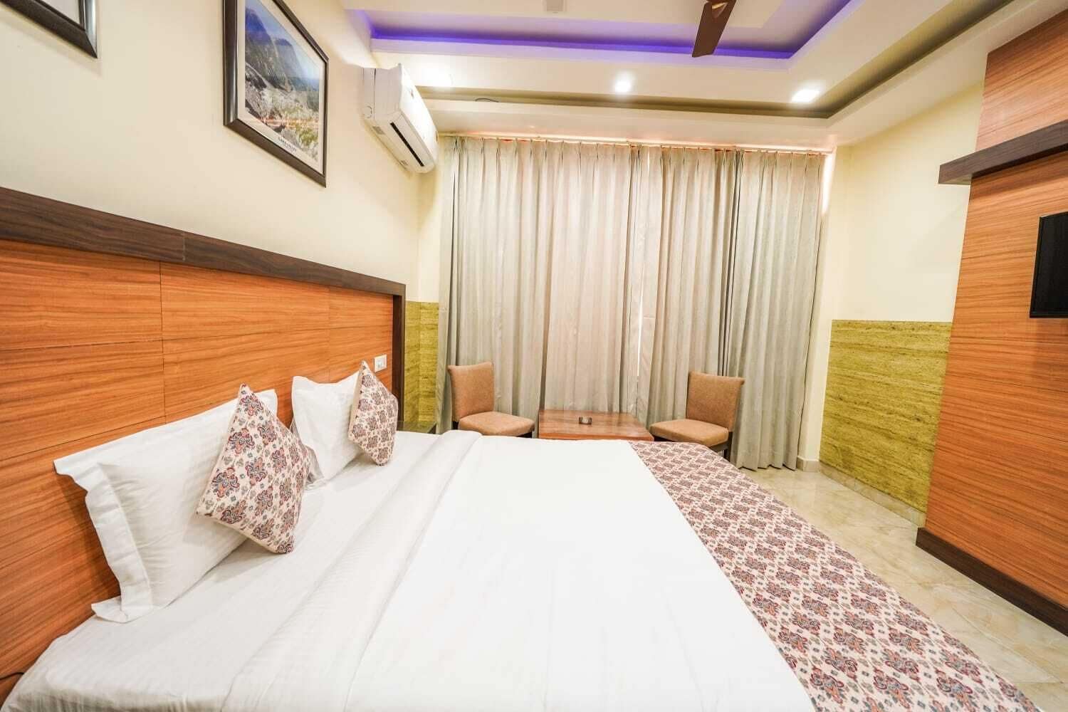 A hotel room with a large bed, a small table, two chairs, a TV, and a window with curtains.
