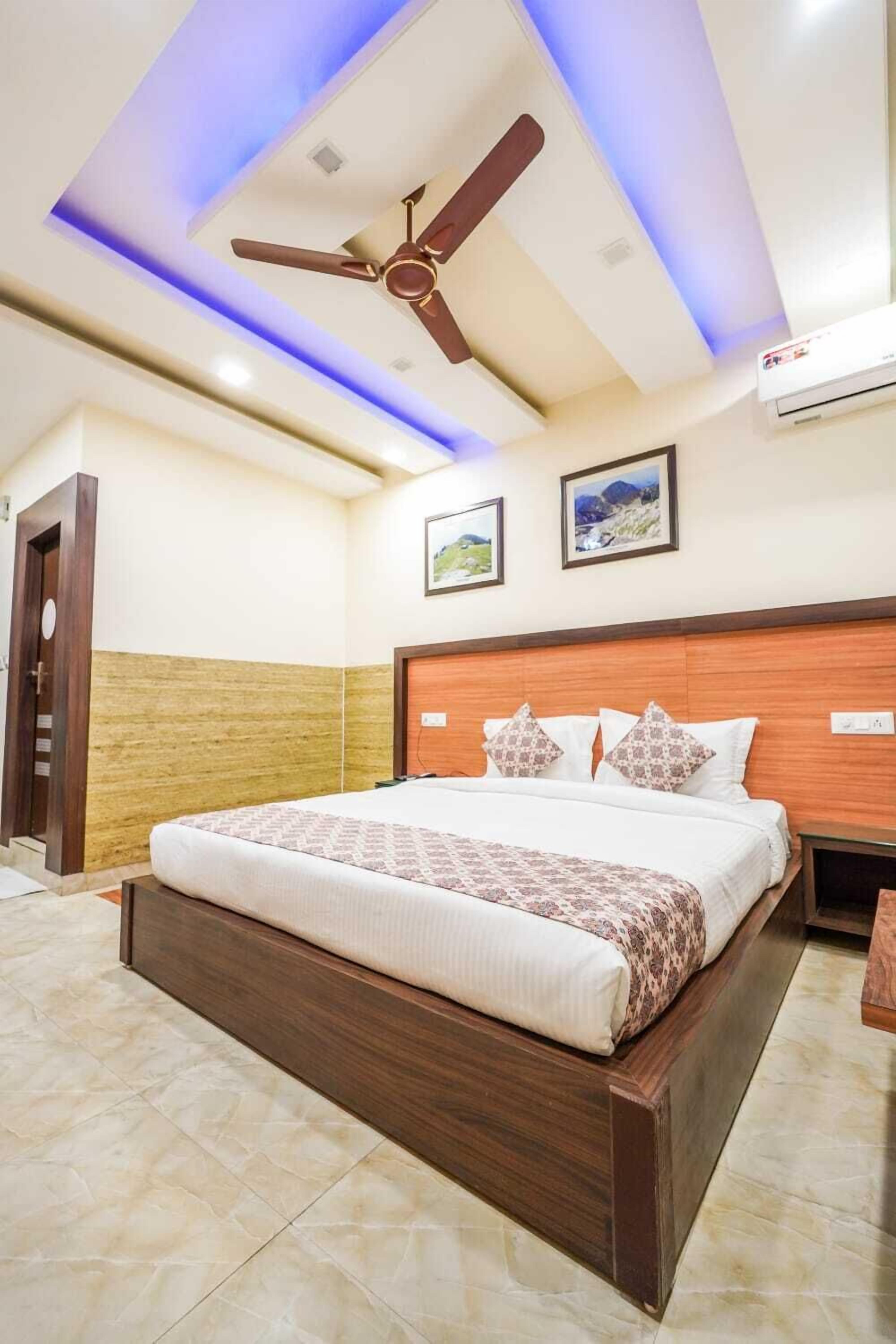 Habitación de hotel con cama, ventilador de techo, aire acondicionado y cuadros en la pared.