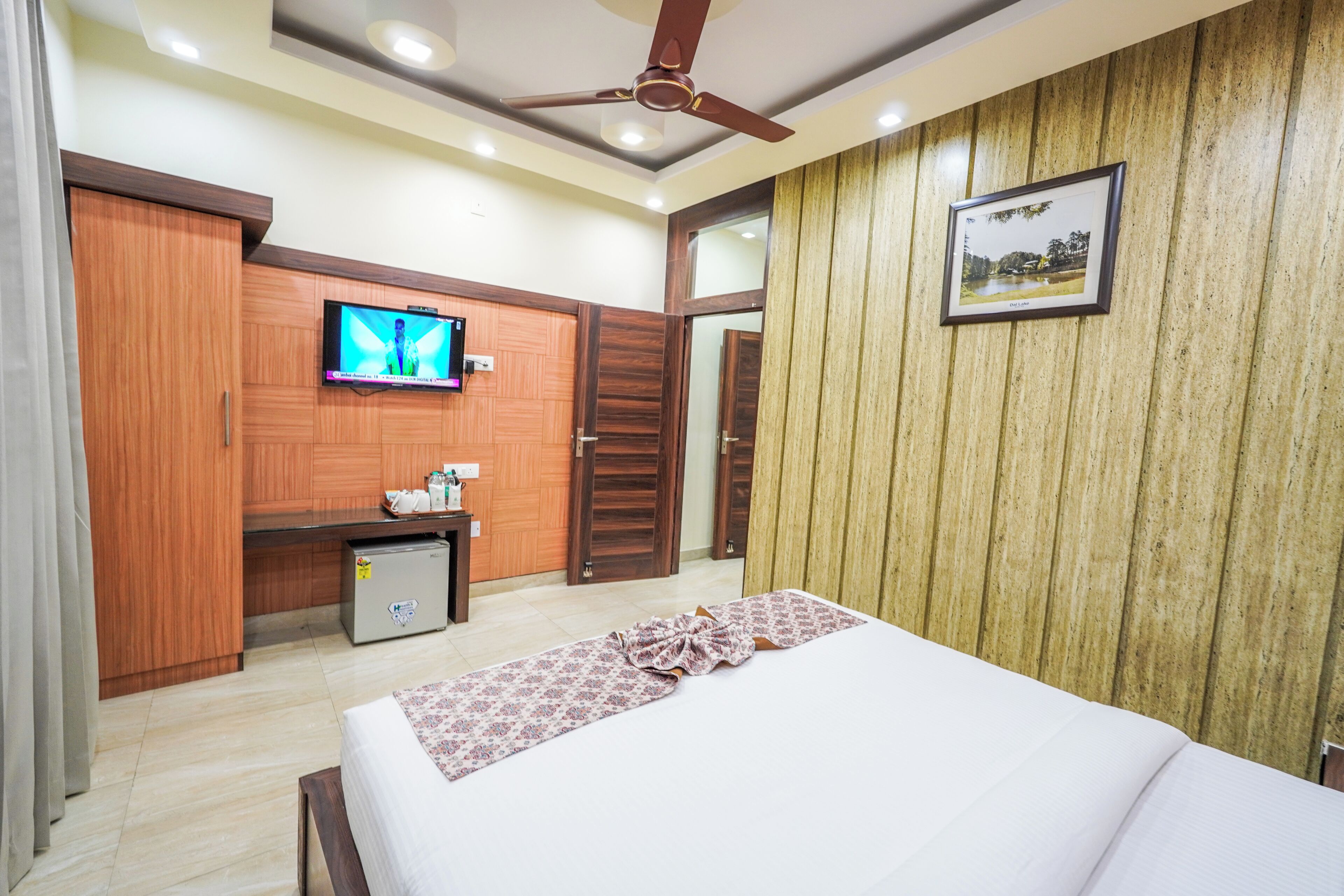 A hotel room with a bed, a television, a small refrigerator, and wooden paneling on the walls.