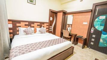 A hotel room with a large bed, a desk, a chair, a wardrobe, and a bathroom door.
