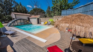 Una piscina con techo de paja y sillas de descanso.