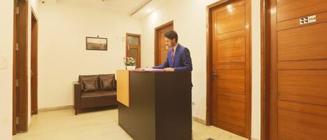 A reception area with a wooden reception desk, a brown leather sofa, and a potted plant.