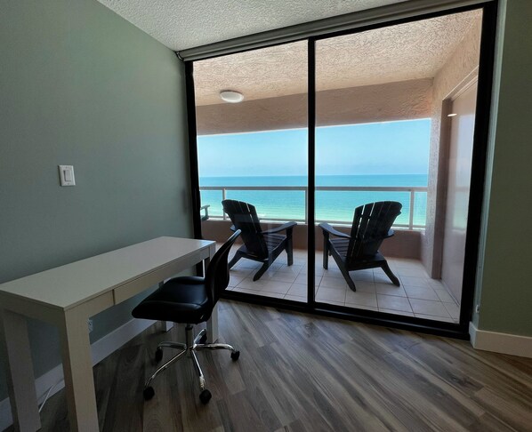 A room with a desk, two chairs, and a large sliding glass door leading to a balcony with a view of the ocean. - Luxury & Sky High views of Sand Key! (Clearwater)