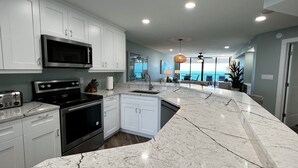 Een moderne keuken met witte kasten, een groot eiland met een spoelbak en uitzicht op de oceaan door grote ramen.