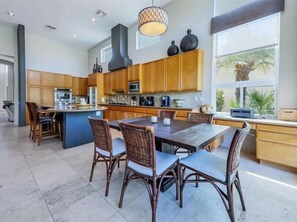 A modern kitchen with wooden cabinets, a central island, and a dining area with wicker chairs.