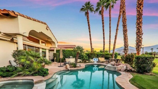 A pool area with a curved design, palm trees, and a building with a tiled roof.