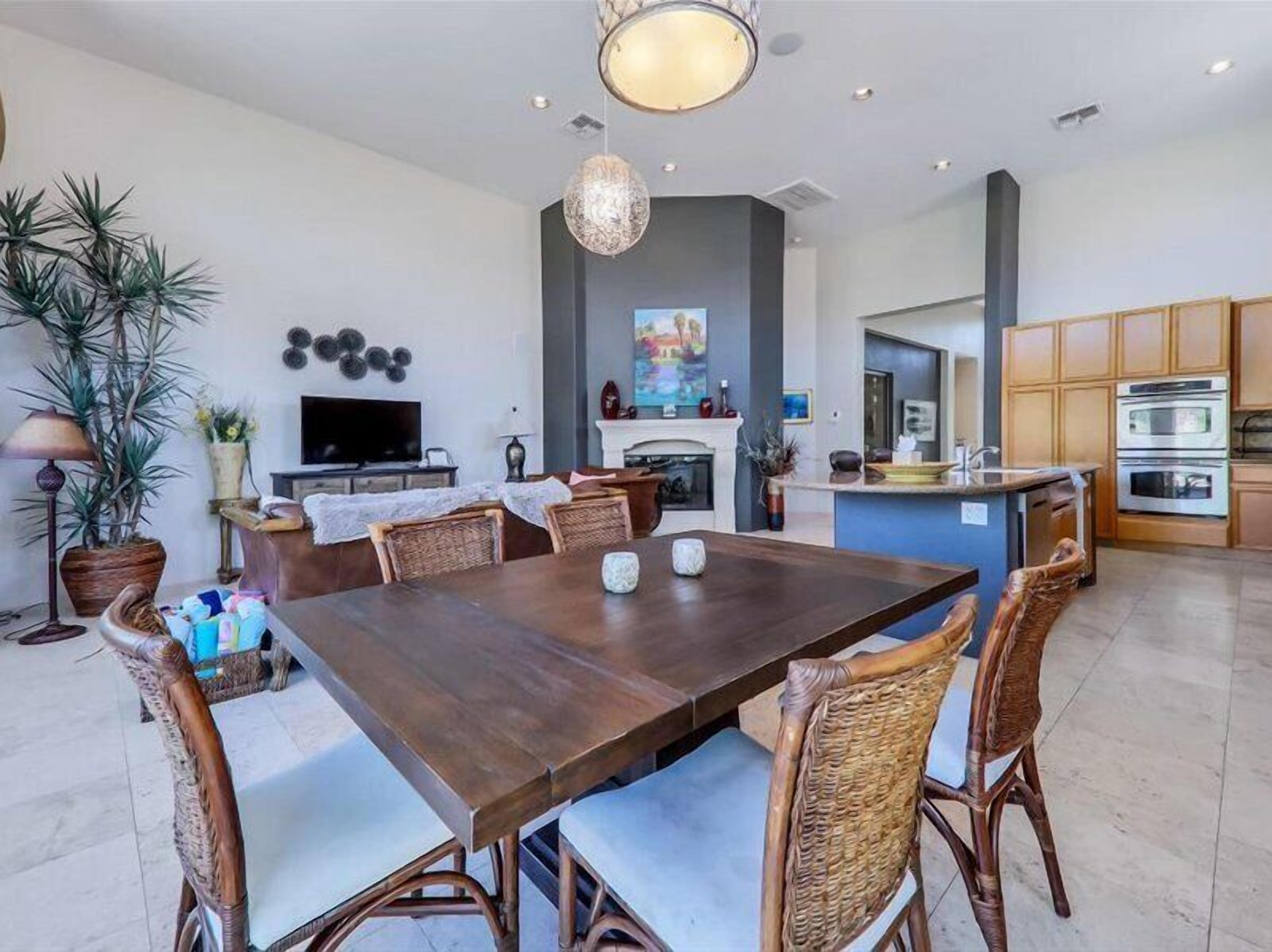 A modern kitchen with a dining area, featuring a large wooden table, wicker chairs, and a central island with a sink.