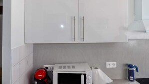Une cuisine avec des meubles blancs, un four à micro-ondes, une machine à café rouge, un rouleau d’essuie-tout et une bouteille d’eau bleue.