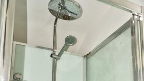 Une cabine de douche fermée par des parois en verre, dotée d’un pommeau de douche à main, d’un robinet mural et d’une molette de réglage.