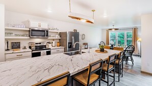 Una cocina moderna con encimera de mármol, electrodomésticos de acero inoxidable y un comedor con sillas de madera.