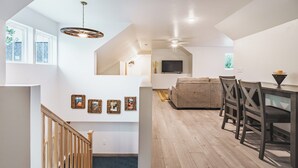 Amplia sala de estar con techo alto, piso de madera, una escalera y un comedor con televisor y mesa.