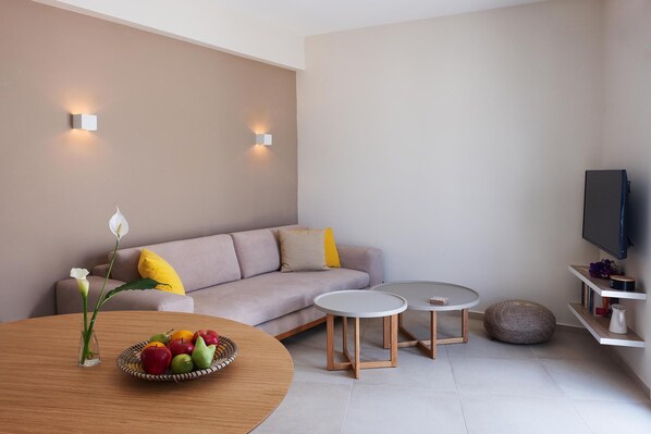 A modern living room with a sofa, two round tables, a fruit bowl, and a television.
