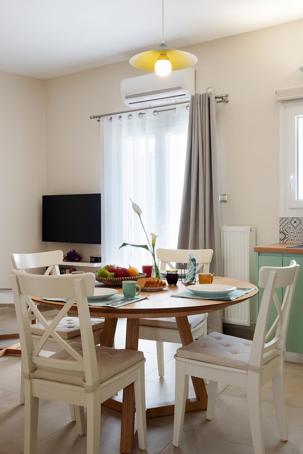 Un coin repas comprenant une table ronde, quatre chaises, un téléviseur à écran plat et une fenêtre avec des rideaux.