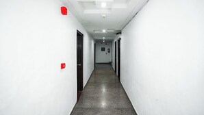 Un couloir étroit et bien éclairé, aux murs blancs et au sol ciré, qui mène à une porte au fond.