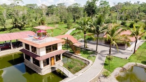 A two-story building with a red roof, surrounded by a pond and palm trees. - Hotel Magic Paradise (Nueva Loja)
