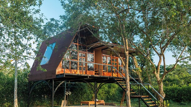 A treehouse with a wooden deck, a staircase, and a bench. - Hotel Magic Paradise (Nueva Loja)