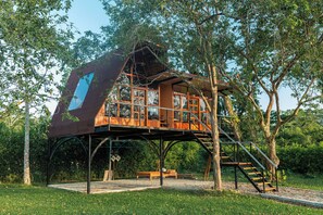 Een boomhut met een houten terras, een trap en een bankje.
