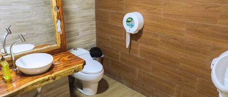 A bathroom with a wooden vanity, a sink, a toilet, and a hand dryer.