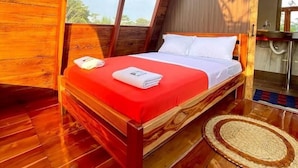 A wooden-framed bed with a red bedspread and white pillows in a room with wooden floors and a large window. - Hotel Magic Paradise (Nueva Loja)