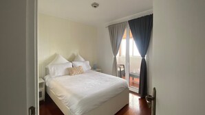 Een slaapkamer met een groot bed, een nachtkastje, een stoel en een schuifdeur die leidt naar een buitenruimte.