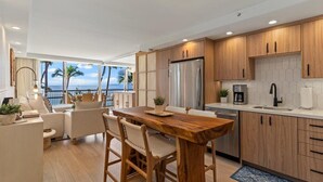 Eine moderne Küche mit Holzschränken, einem Edelstahlkühlschrank und einer Kaffeemaschine. Es gibt einen Essbereich mit Holztisch und Stühlen.