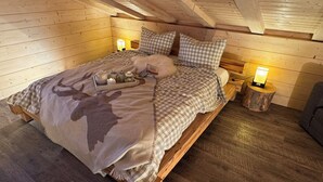 Une chambre confortable dans un chalet en bois, avec un lit, une literie à carreaux, une couverture ornée de motifs de cerfs, des tables de chevet avec des lampes et une atmosphère rustique.
