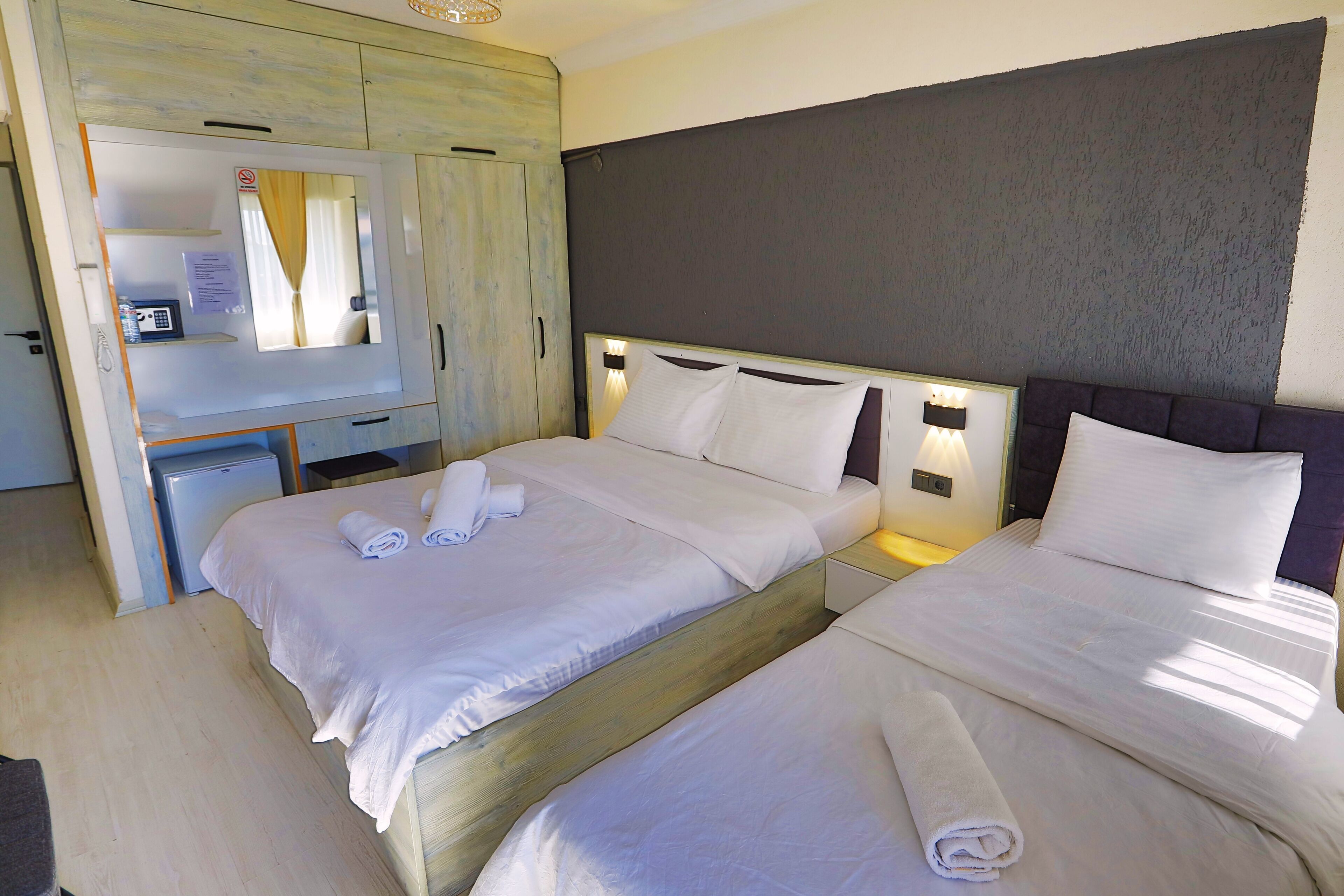 A hotel room with two beds, a wardrobe, a desk with a computer, and a mirror.