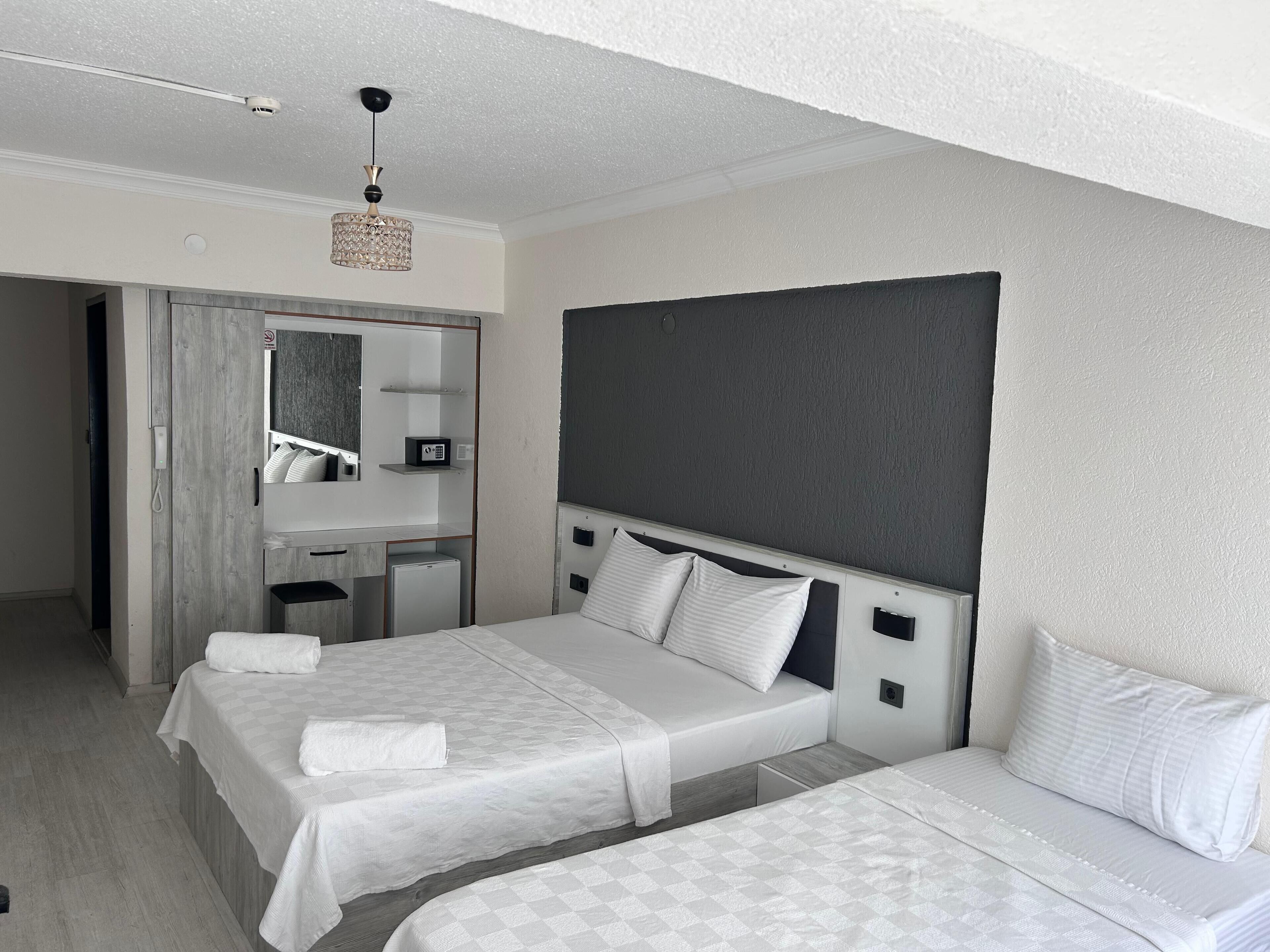 A hotel room with two beds, a desk, a mirror, and a small refrigerator.
